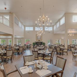 A spacious and elegantly designed dining room with multiple tables, chairs, large chandeliers, and abundant natural light.