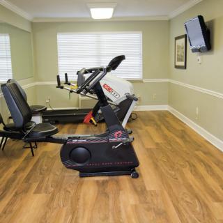 A small exercise room with a stationary bike, treadmill, and a wall-mounted television.