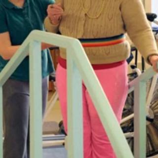 A person receiving assistance during physical therapy to practice walking up stairs.