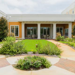 A beautifully landscaped garden with a patio and lush green lawn in front of a building.