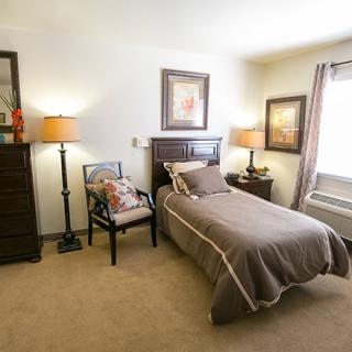 A cozy bedroom with a single bed, dresser, and soft lighting from two lamps.