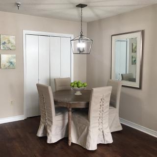 A cozy dining room with a round table, covered chairs, and a modern chandelier.
