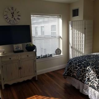 A cozy bedroom with a television, dresser, and sunlight streaming through the window.
