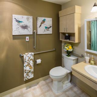A well-decorated bathroom featuring a toilet, sink, and mirror, complemented by artwork and fresh flowers.