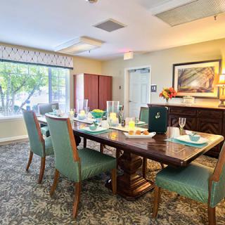 A well-decorated dining room with a large table and chairs, featuring natural light from a broad window.