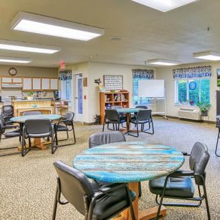 A brightly lit community center meeting room with tables and chairs arranged for group activities.
