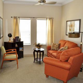 A cozy living room with an orange sofa, a chair, and large windows with curtains.
