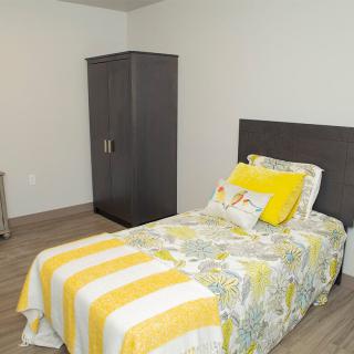 A minimalist bedroom with a single bed featuring yellow bedding and a dark wardrobe.