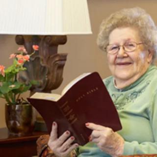 An elderly woman sitting in a cozy living room, smiling while reading a book.