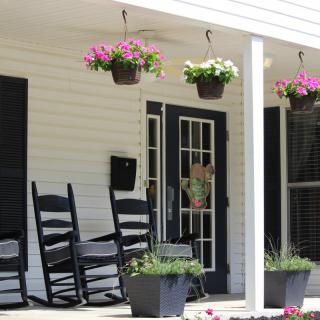 A cozy front porch with black rocking chairs, hanging flower baskets, and potted plants.