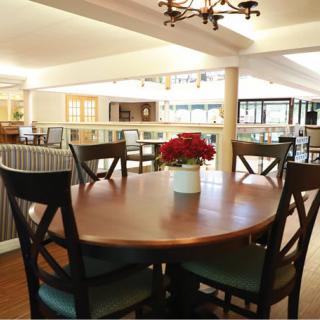 A cozy dining area with a round wooden table surrounded by chairs, featuring a central flower arrangement.