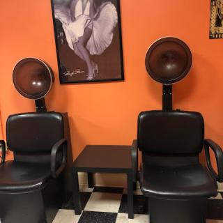 A cozy salon space featuring hair styling chairs and dryers against an orange wall.