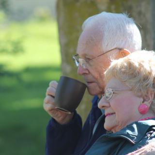 An elderly couple enjoys a peaceful moment outdoors, sipping coffee and embracing nature.