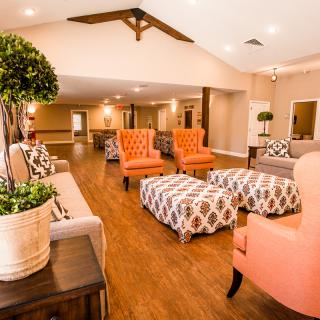 A cozy lounge area featuring orange armchairs, patterned ottomans, and potted plants on a hardwood floor.
