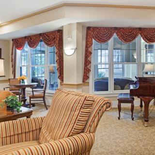 A cozy living room with a piano and comfortable seating, featuring large windows and elegant decor.