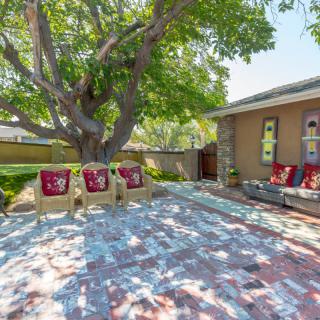 A cozy backyard patio with outdoor seating under the shade of a large tree.