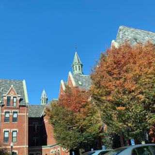 A picturesque view of a historic college building framed by vibrant autumn foliage under a clear blue sky.