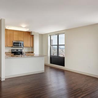 A modern apartment with an open floor plan featuring a kitchen and living area with hardwood floors and large windows.