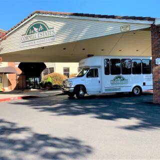A shuttle bus is parked under the awning at the entrance of a building with signage.