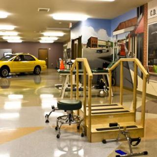 A physical therapy room featuring rehab equipment and a yellow car, designed to create a supportive environment for recovery.