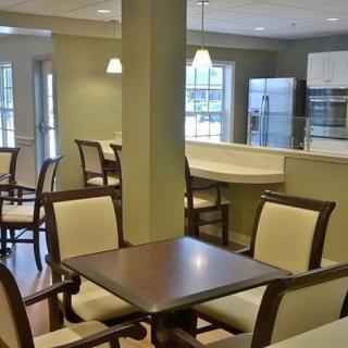 A modern dining area with wooden tables and chairs, adjacent to an open kitchen.