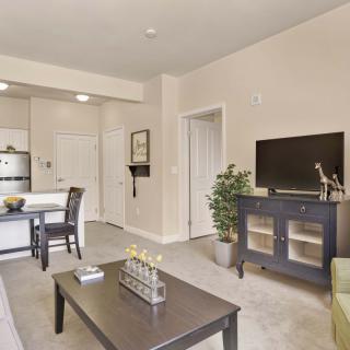 A modern living room with a view into the kitchen area, featuring a television, coffee table, and dining set.