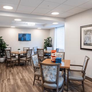 A modern dining area with several tables and chairs, decorated with plants and artwork on the walls.