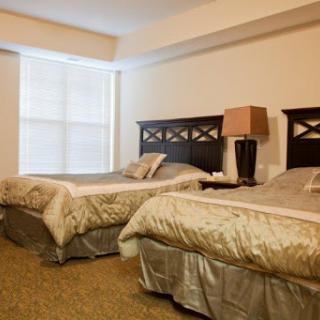 A cozy hotel bedroom featuring two twin beds with elegant bedding and a stylish lamp beside the window.