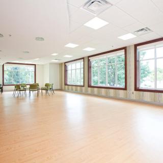 A spacious room with large windows, wooden flooring, and a group of chairs near the window.