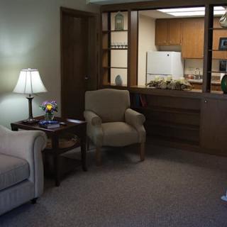 A cozy living room with a sofa, chair, and a view into the kitchenette.