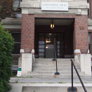 The image shows the entrance of a brick building with stairs leading up to a doorway.