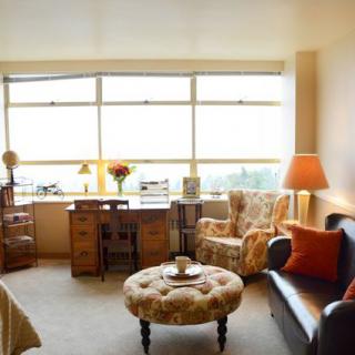 A cozy living room with a sofa, armchair, desk, and large window.