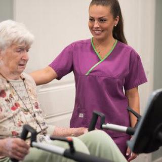 A nurse assists an elderly woman during a rehabilitation exercise session.