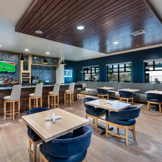 A modern restaurant interior with a bar area, featuring stylish seating and a wooden ceiling.