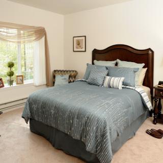 A cozy and elegantly decorated bedroom featuring a beautifully made bed with blue bedding and soft lighting from the window.