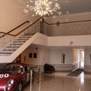 A classic car displayed in an elegant lobby with a staircase and chandelier.
