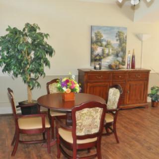 A cozy room setup featuring a round table with chairs, a decorative plant, and a sideboard with a painting above it.