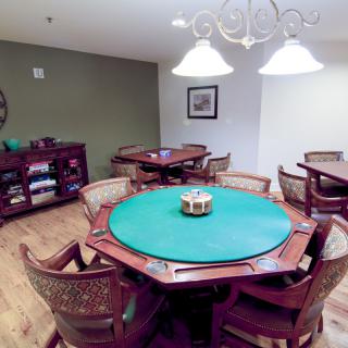 A cozy game room featuring a poker table surrounded by wicker chairs under warm lighting.