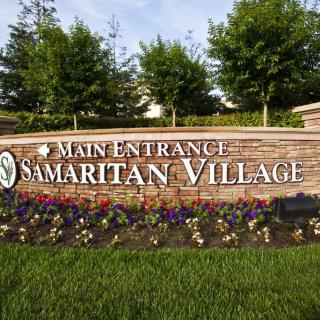 Main entrance sign for Samaritan Village surrounded by landscaped flowers and greenery.