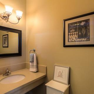 A well-lit bathroom featuring a sink, a mirror, and framed artwork on the wall.