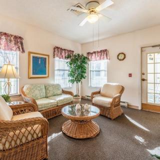 A cozy living room with wicker furniture and a coffee table, featuring large windows and an indoor plant.