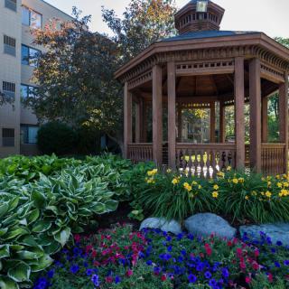 A scenic view of a wooden gazebo surrounded by a vibrant garden with blooming flowers and lush greenery.