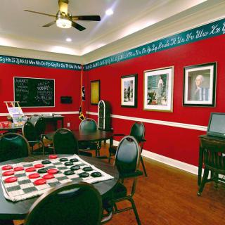 A cozy game room with red walls, featuring tables set up for checkers and decorated with artwork.