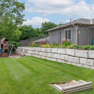 A backyard with a well-maintained lawn, retaining wall, and playground set.