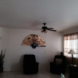 A cozy living room with armchairs, a ceiling fan, and a decorative wall piece.