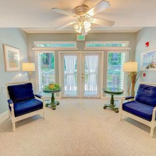 A cozy living room with two blue chairs, a central table, and large windows in a bright setting.