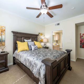 A cozy bedroom with a large wooden bed, decorative pillows, ceiling fan, and wall art.