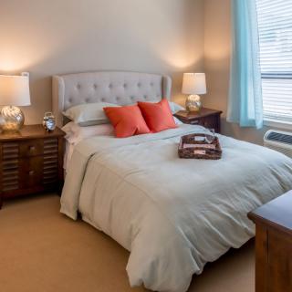 A cozy bedroom with a neatly made bed, adorned with coral pillows and bedside lamps.