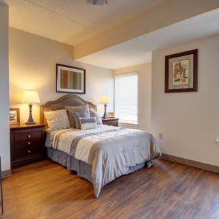 A cozy bedroom with a neatly made bed, framed artwork, and ample natural light.