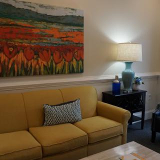 A cozy living room with a yellow sofa, vibrant artwork, and a side table with a lamp.